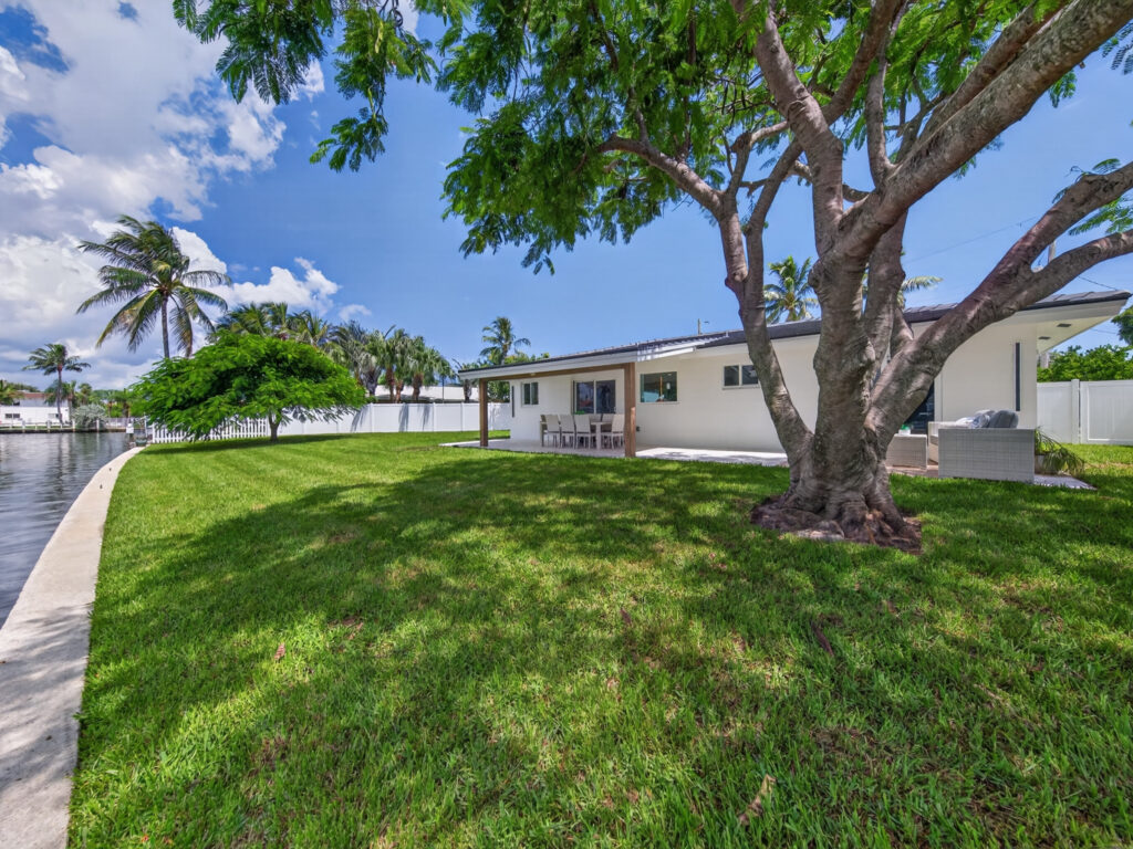 Fenced rear lawn running down to the seawall, with the house and shade tree